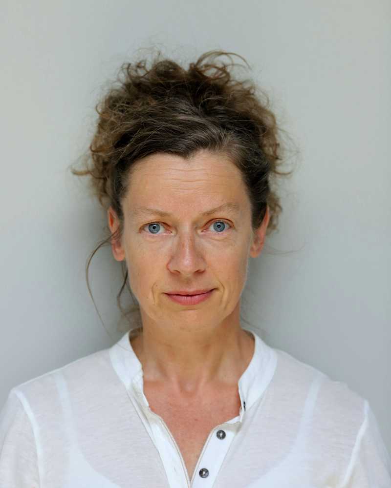 Sinéad Rushe Headshot - White woman with blue eyes and brown hair wearing a white top against a pale background.