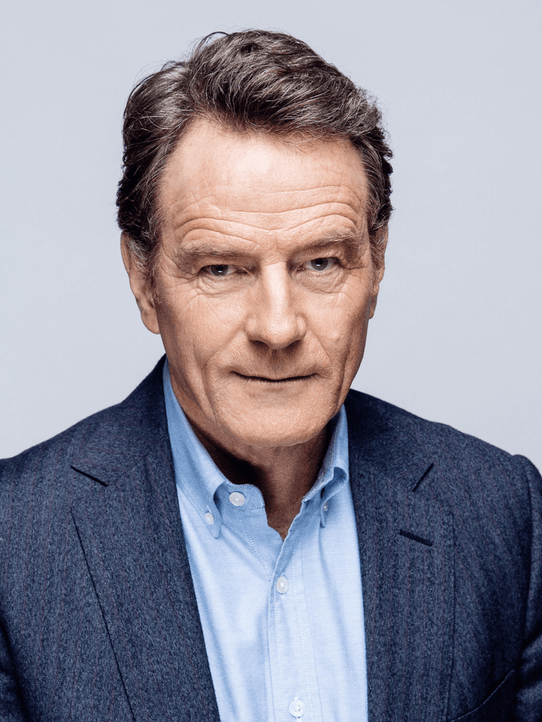 Headshot of Bryan Cranston, a man with neatly styled hair wearing a tailored dark blazer over a light blue shirt, set against a plain light grey background.