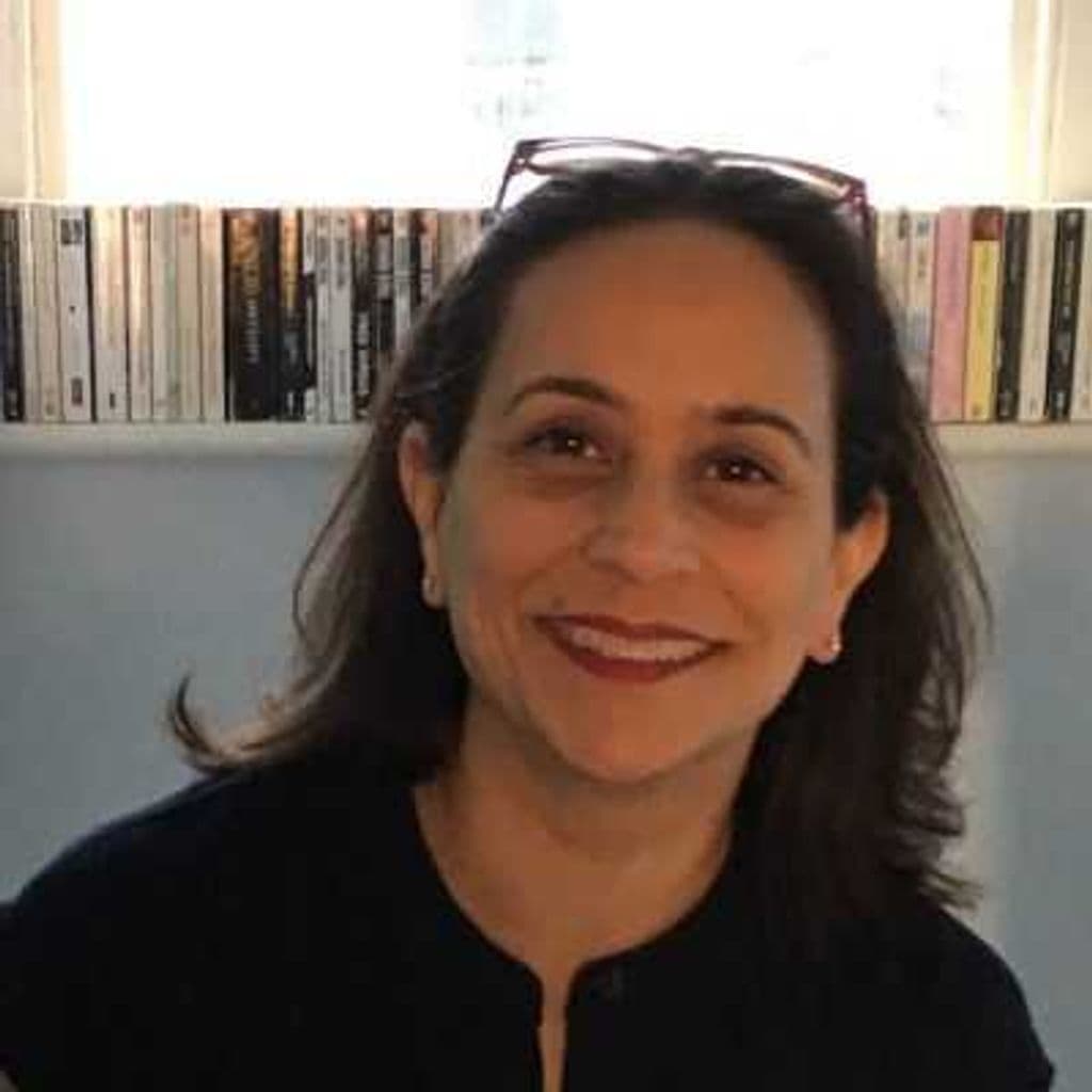 Photo of Clare Annamalai. Brown haired woman, wearing red lipstick with glasses on top of her head.