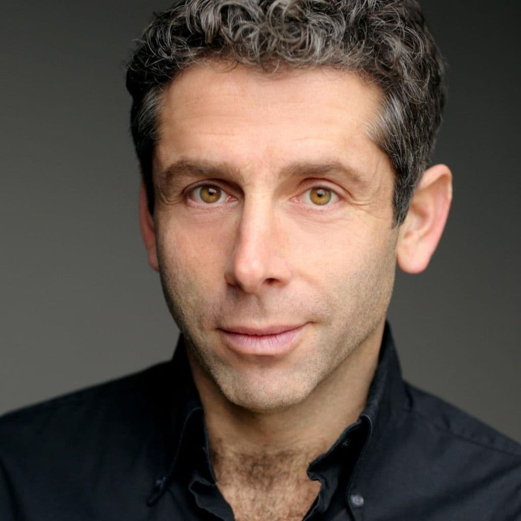 Elliot Levey headshot - black shirt, with dark background