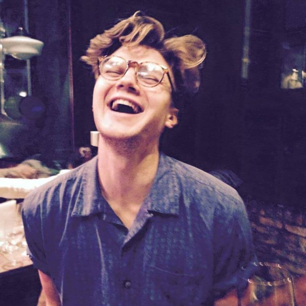 Casting Director, Jacob Sparrow, laughing. Dressed in a blue shirt, with spectacles and mid-length brown hair.