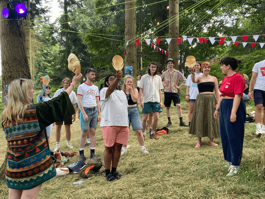 A group of young people doing a mask workshop with Masterclass member Georgie, at Latitude Festival out in the woods.