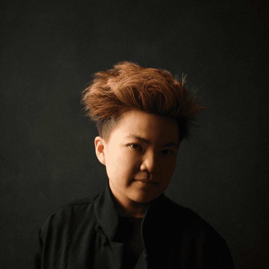 Headshot of Nicola T Chang, who wears a black shirt against a dark background, creating a dramatic silhouette.