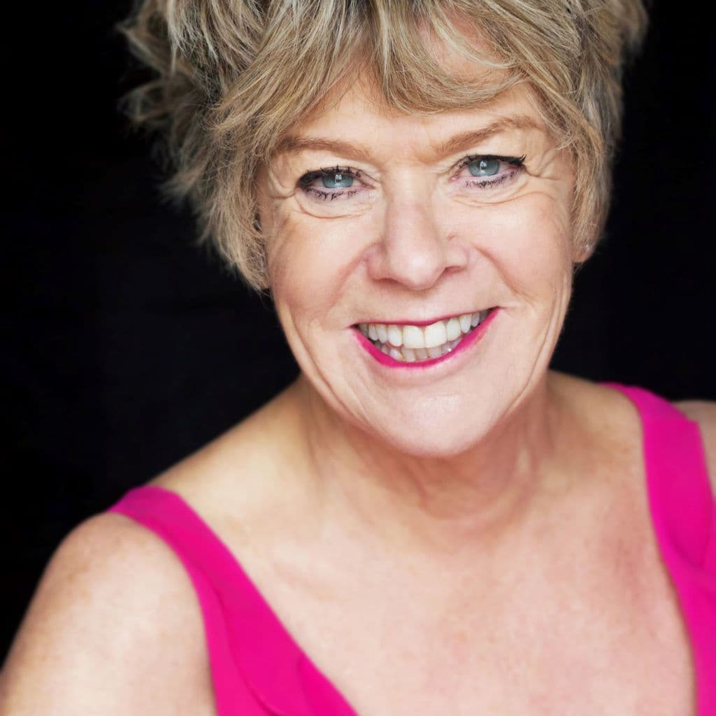 Rosemary Ashe headshot, wearing a bright pink top against a black background.
