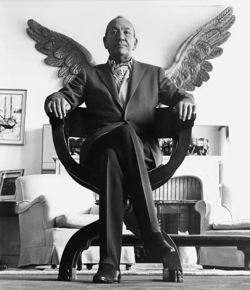 Noel Coward - 1963, sat on chair with wings behind him