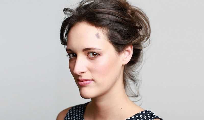 Headshot of Phoebe Waller-Bridge, in slight profile looking directly into the camera. Wearing a polka dot top with their hair pinned up.