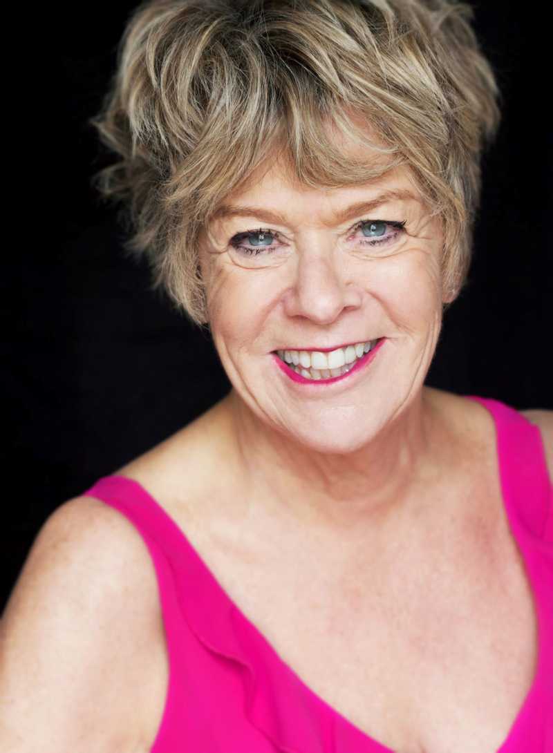Rosemary Ashe headshot, wearing a bright pink top against a black background.