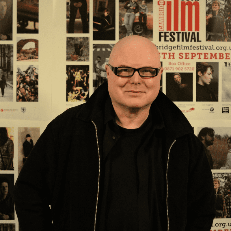 Philip Ridley at the Cambridge Film Festival in a black shit and hoody, wearing black framed glasses. Philip is a white man, with bald head.